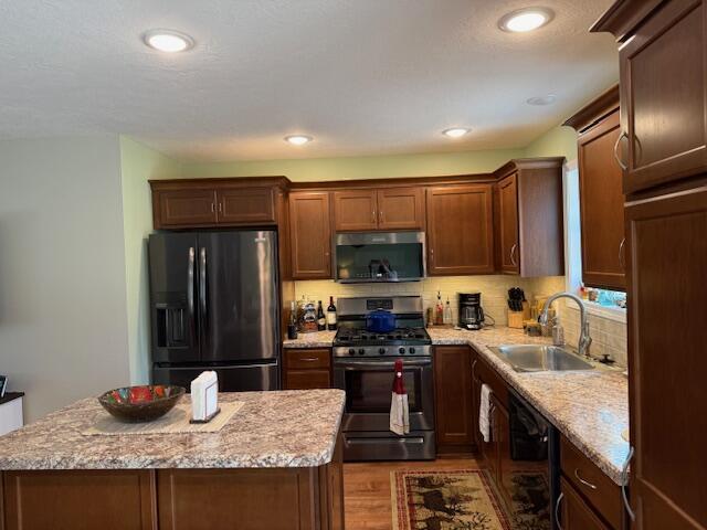 kitchen featuring a sink, a center island, wood finished floors, backsplash, and black appliances