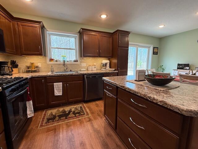 kitchen featuring decorative backsplash, wood finished floors, light stone countertops, a sink, and black appliances