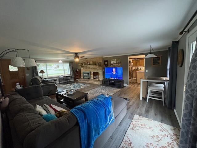 living room featuring a ceiling fan, baseboards, wood finished floors, and a fireplace