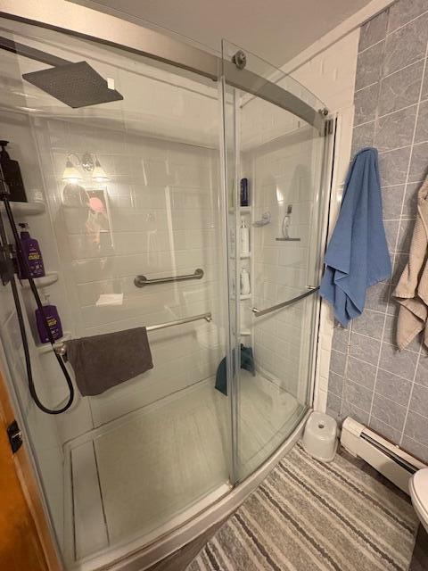 full bath with toilet, tile walls, baseboard heating, and a stall shower