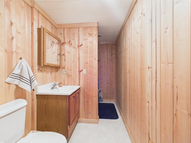 bathroom with vanity, wood walls, and toilet