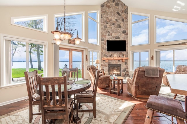 dining space with a water view, high vaulted ceiling, wood finished floors, and a fireplace