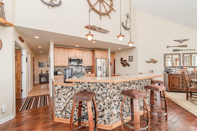 kitchen featuring appliances with stainless steel finishes, a kitchen breakfast bar, hardwood / wood-style floors, and a towering ceiling