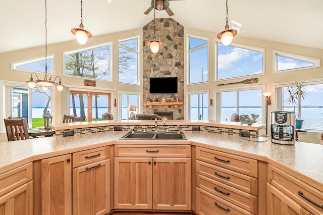 kitchen with ceiling fan, a sink, light countertops, high vaulted ceiling, and a stone fireplace