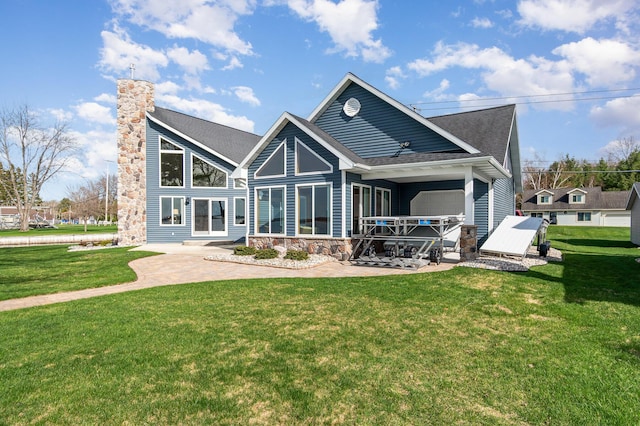 rear view of property featuring stone siding, a patio, a chimney, a shingled roof, and a yard