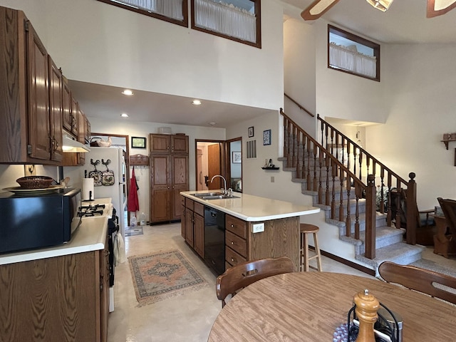 kitchen featuring a high ceiling, light countertops, under cabinet range hood, a sink, and black appliances