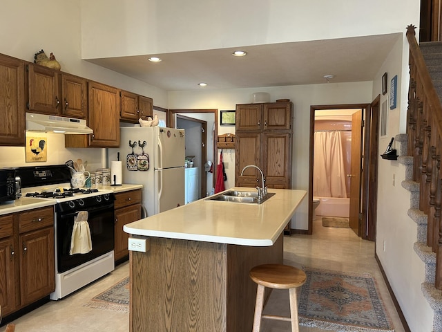 kitchen featuring a sink, light countertops, range with gas stovetop, freestanding refrigerator, and under cabinet range hood