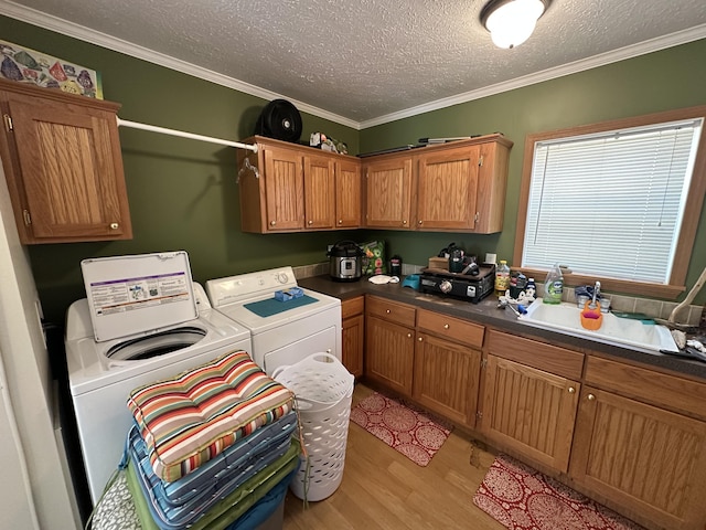 washroom with a textured ceiling, crown molding, washing machine and dryer, light wood-type flooring, and cabinet space