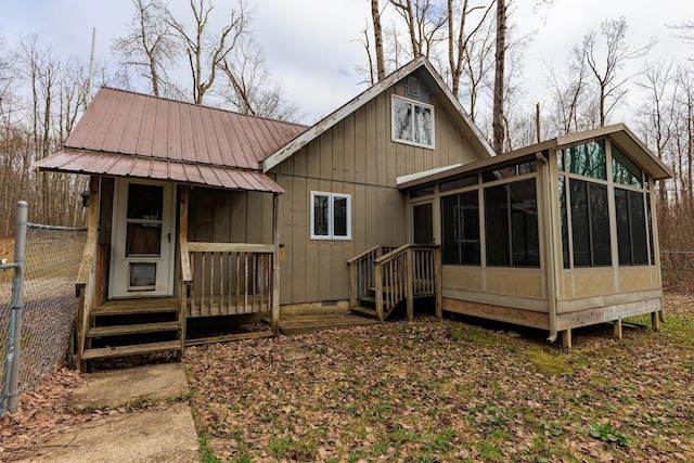rear view of property featuring fence, board and batten siding, a sunroom, and metal roof
