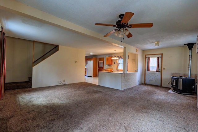 unfurnished living room with stairs, a ceiling fan, light carpet, and a wood stove