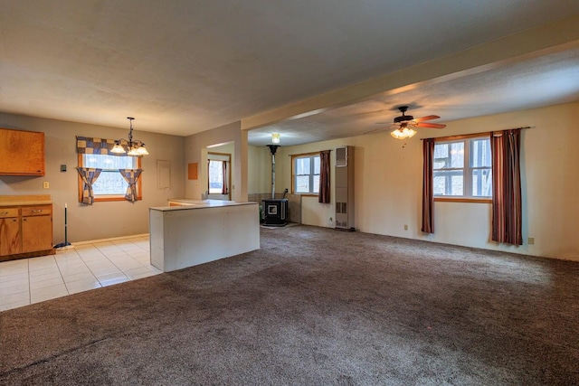 kitchen with light colored carpet, a wood stove, open floor plan, and hanging light fixtures