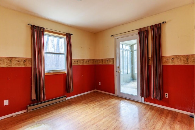 empty room featuring a baseboard heating unit, wainscoting, and light wood finished floors