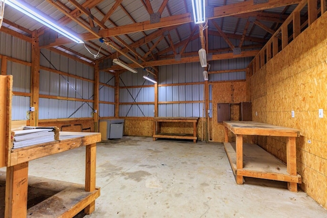 misc room featuring a garage, vaulted ceiling, unfinished concrete flooring, and metal wall