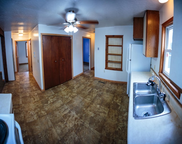 kitchen featuring freestanding refrigerator, baseboards, ceiling fan, light countertops, and a sink