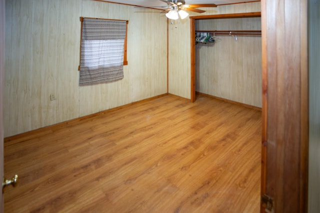 unfurnished bedroom with wooden walls, ceiling fan, a closet, and wood finished floors