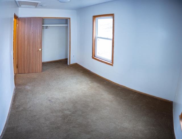 unfurnished bedroom with a closet, carpet flooring, baseboards, and attic access