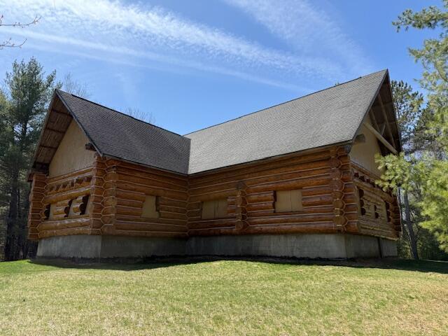 view of home's exterior featuring a lawn, a shingled roof, and log siding
