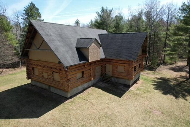 view of front facade with a shingled roof, a front lawn, and log siding