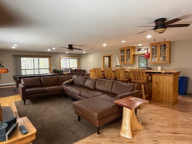 living area with light wood-style floors, a bar, a ceiling fan, and a baseboard heating unit