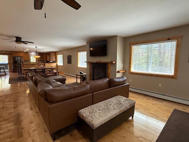 living area with light wood-style floors, ceiling fan, baseboard heating, and a wealth of natural light