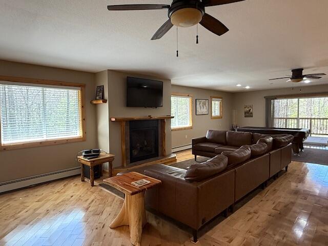 living room with light wood-style floors, a ceiling fan, a baseboard heating unit, and a wealth of natural light