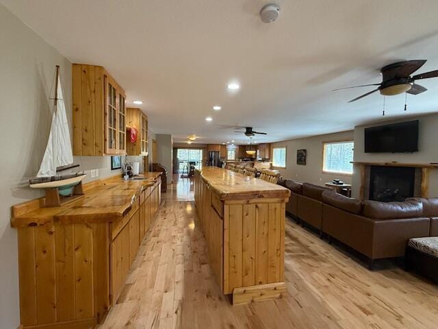 kitchen with ceiling fan, light wood-style floors, a center island, open floor plan, and glass insert cabinets