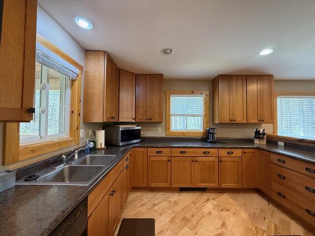 kitchen featuring stainless steel microwave, dark countertops, a sink, and light wood finished floors