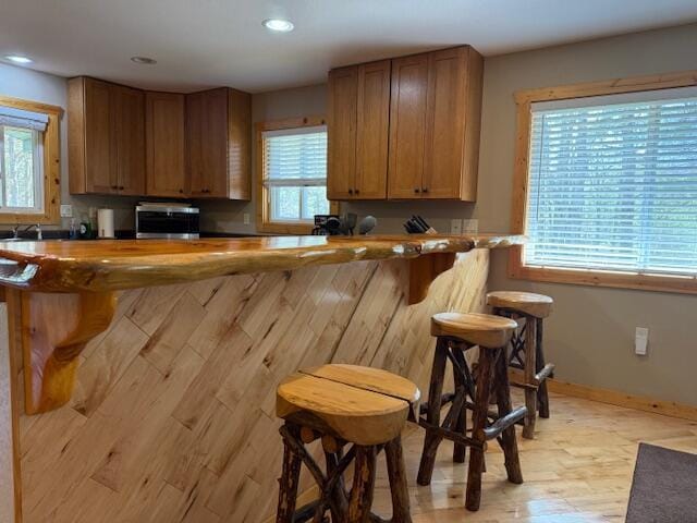 kitchen featuring brown cabinetry, a peninsula, a kitchen bar, recessed lighting, and light wood-style flooring
