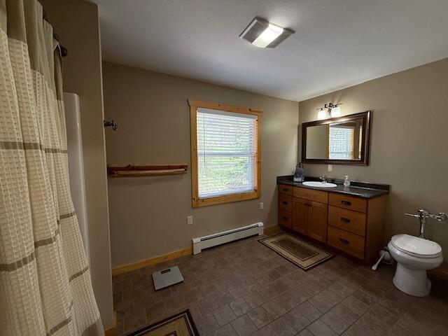 8670 N Everett Rd, Roscommon, MI 48653 - full bath featuring a shower with curtain, vanity, a baseboard radiator, baseboards, and toilet