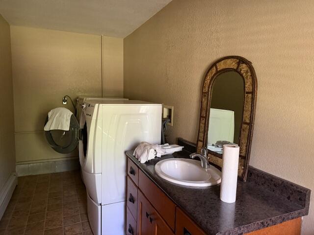bathroom featuring a textured wall, tile patterned flooring, vanity, baseboards, and washer and clothes dryer