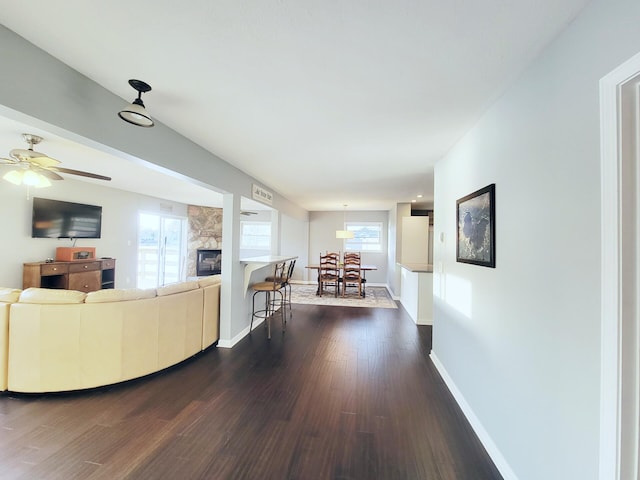 living area featuring a ceiling fan, baseboards, dark wood-style floors, and a fireplace