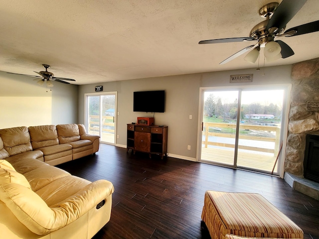 living area with a fireplace, baseboards, ceiling fan, dark wood-type flooring, and a textured ceiling