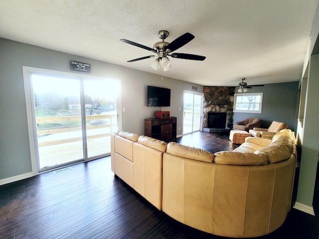 living room with a ceiling fan, baseboards, a stone fireplace, and dark wood-type flooring