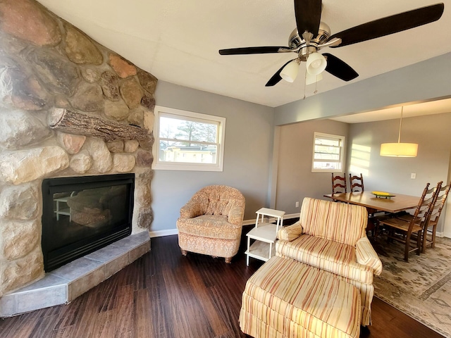 sitting room with baseboards, ceiling fan, a stone fireplace, and wood finished floors