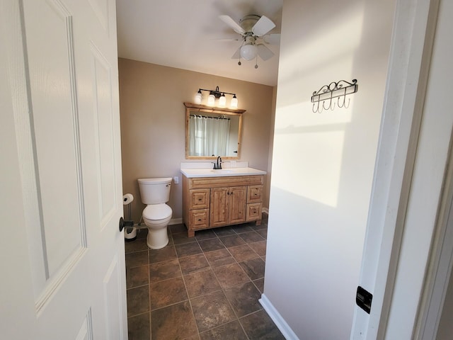 half bathroom with a ceiling fan, stone finish flooring, vanity, baseboards, and toilet