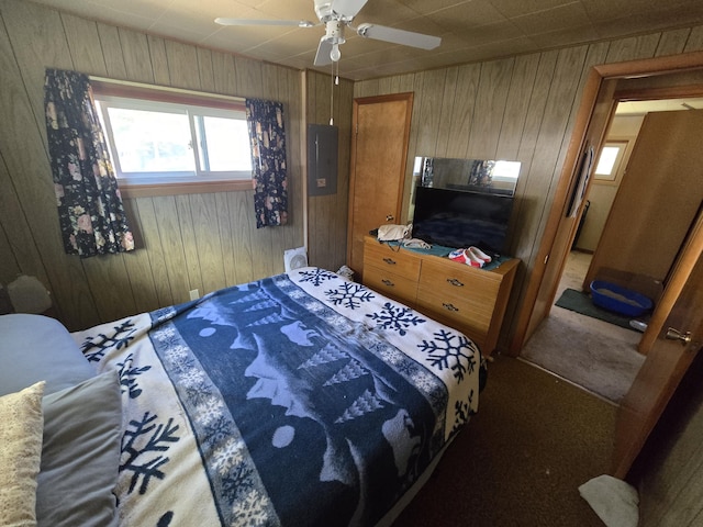 bedroom with carpet floors, wood walls, ceiling fan, and electric panel