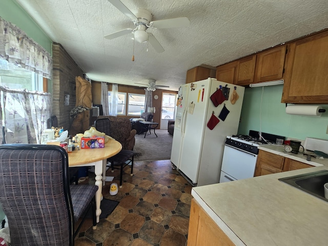 kitchen featuring brown cabinetry, a ceiling fan, light countertops, a sink, and white appliances