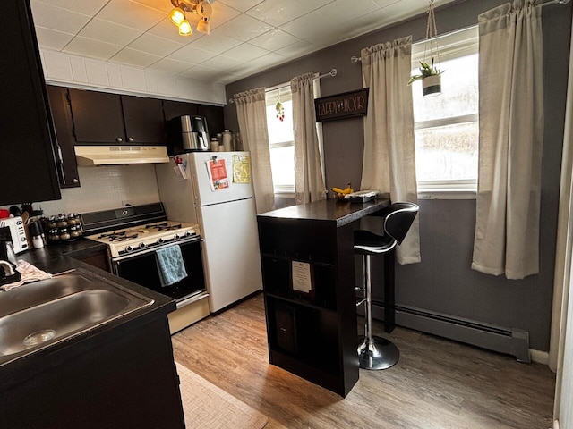 kitchen featuring a healthy amount of sunlight, a sink, a baseboard heating unit, under cabinet range hood, and white appliances