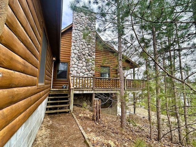view of side of home featuring a chimney, log veneer siding, and a deck