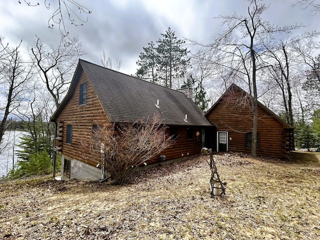 view of home's exterior with log exterior, roof with shingles, and a chimney