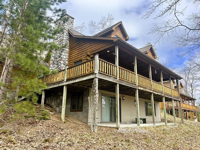 back of house with a chimney, faux log siding, and a deck