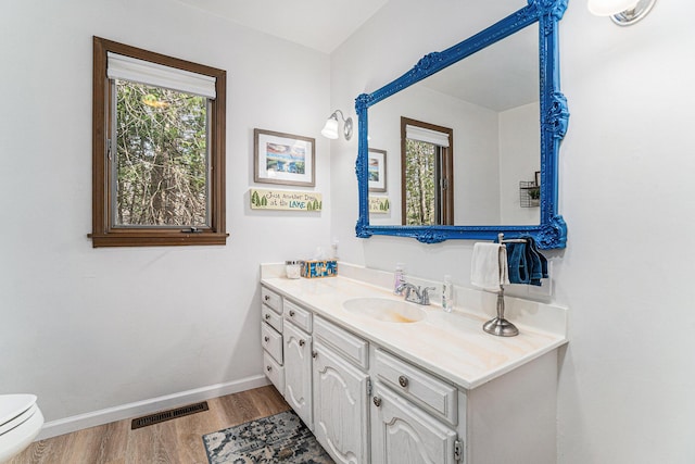 bathroom with vanity, toilet, baseboards, wood finished floors, and visible vents