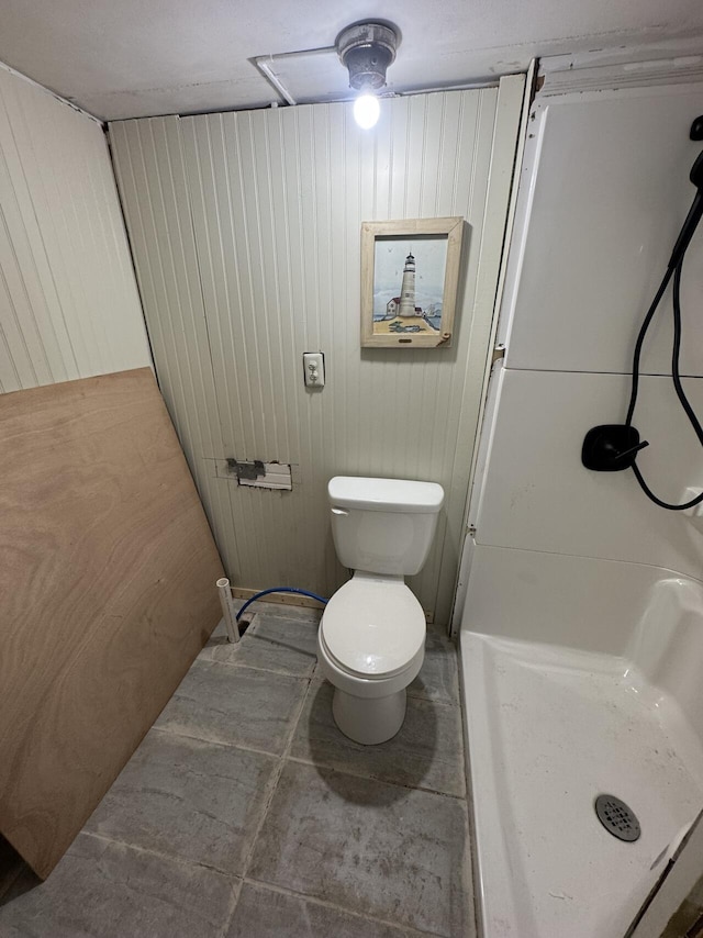 bathroom featuring toilet, wood walls, and a shower stall