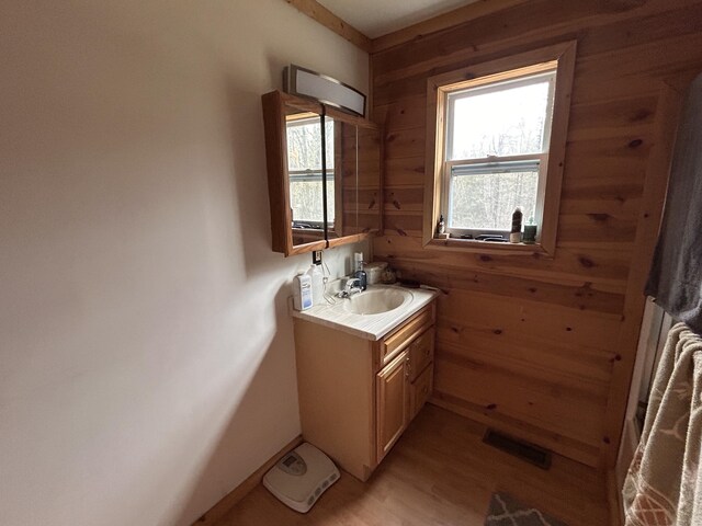 bathroom featuring vanity, visible vents, wood finished floors, baseboards, and wooden walls