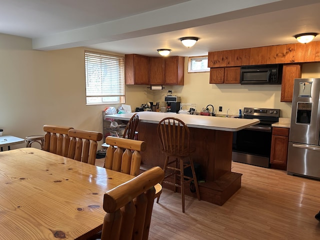 kitchen with brown cabinetry, a breakfast bar area, light wood-type flooring, light countertops, and stainless steel appliances