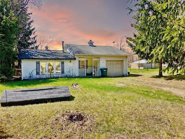 back of property at dusk with a garage, a yard, and driveway