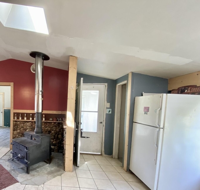 kitchen with freestanding refrigerator, light tile patterned flooring, vaulted ceiling, and a wood stove
