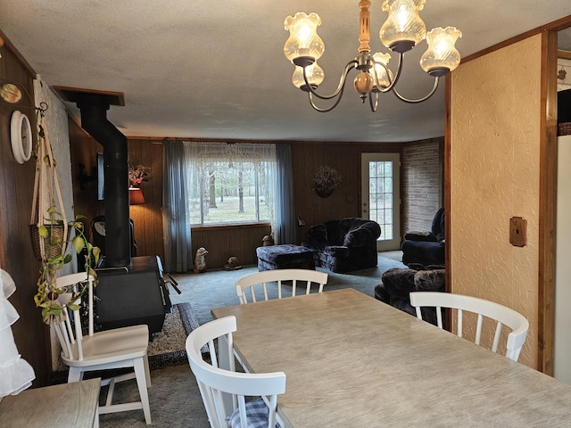 carpeted dining space with a wood stove, a textured wall, wood walls, and a notable chandelier