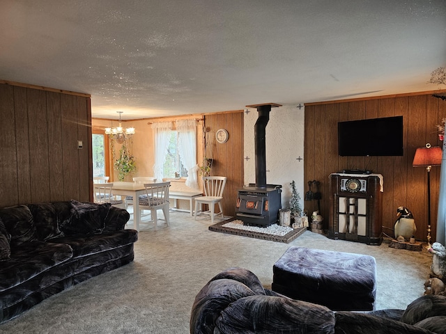 carpeted living room featuring a wood stove, wood walls, a chandelier, and a textured ceiling