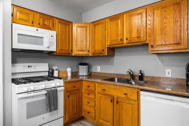 kitchen featuring a sink, brown cabinetry, white appliances, and dark countertops